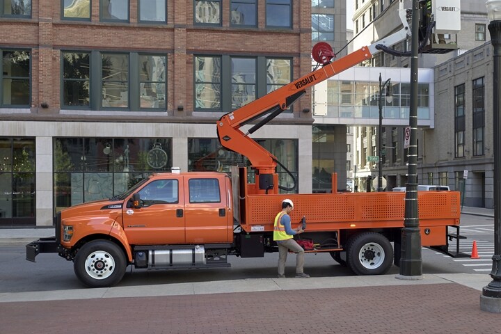 Un trabajador arregla una farola en una calle de ciudad con la mejora de plataforma elevadora en una Ford F-750 Crew Cab 2024 en Tangier Orange
