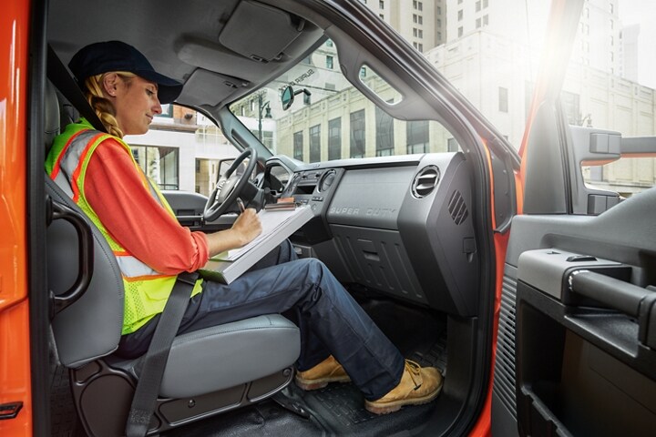 Una trabajadora escribiendo en un sujetapapeles en el asiento del pasajero de una Ford F-750 Crew Cab 2024 en Tangier Orange