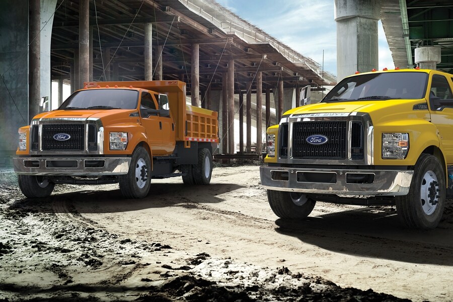 Los modelos Ford F-750 2024 con mejoras de camioneta volcadora estacionados uno junto al otro cerca de un paso elevado