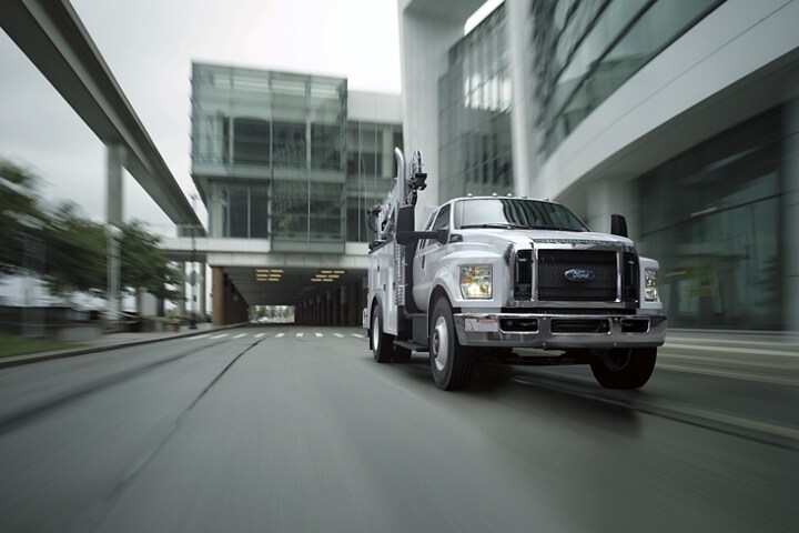 Una Ford F-750 SuperCab 2024 con mejora mecánica en Oxford White circulando cerca de edificios grandes