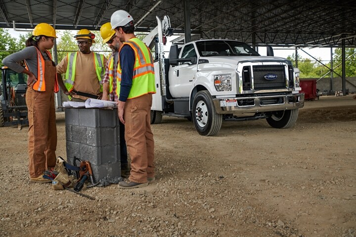 Unos trabajadores reunidos junto a una Ford F-750 SuperCab 2024 con mejora mecánica en Oxford White en el fondo