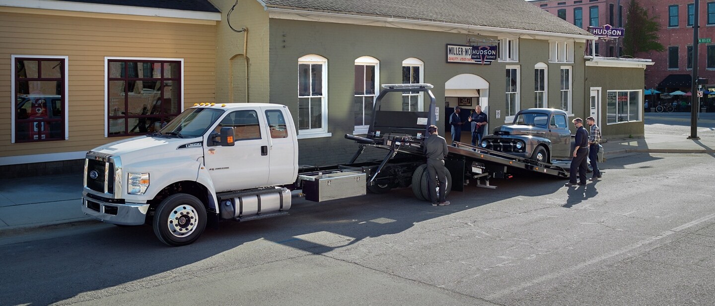 2026 Ford F-650 shown in Oxford White with rollback body flatbed loading a pickup truck into the bed