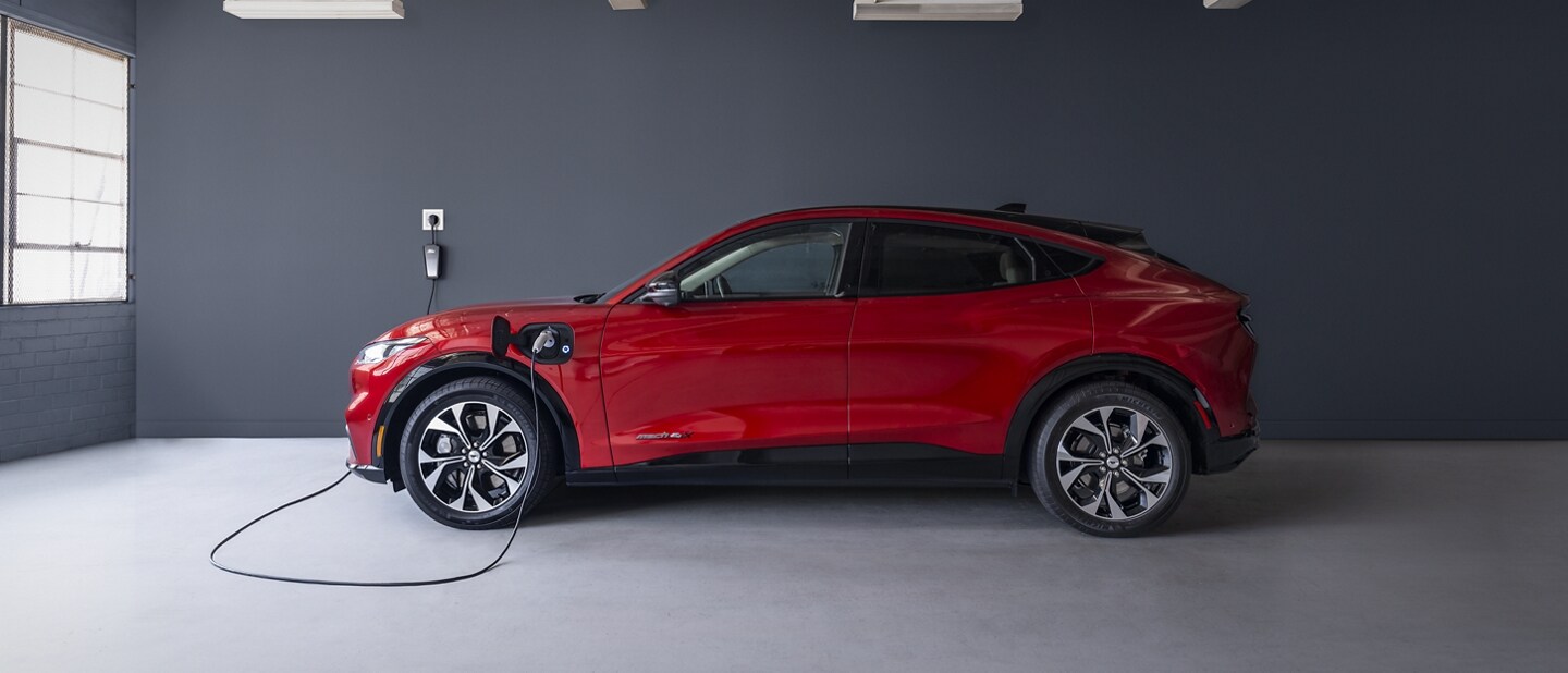 Vista lateral de la Ford Mustang Mach-E® 2023 enchufada a un cargador doméstico en un garaje