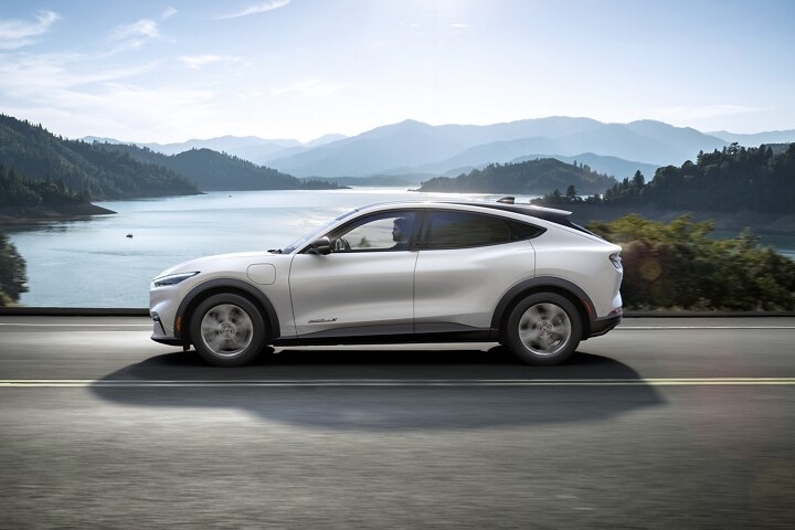 Una Ford Mustang Mach-E® 2023 andando por una carretera junto a las montañas y un lago