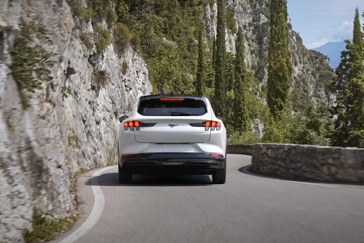 Vista trasera de una Ford Mustang Mach-E® 2023 andando por una carretera en un entorno montañoso