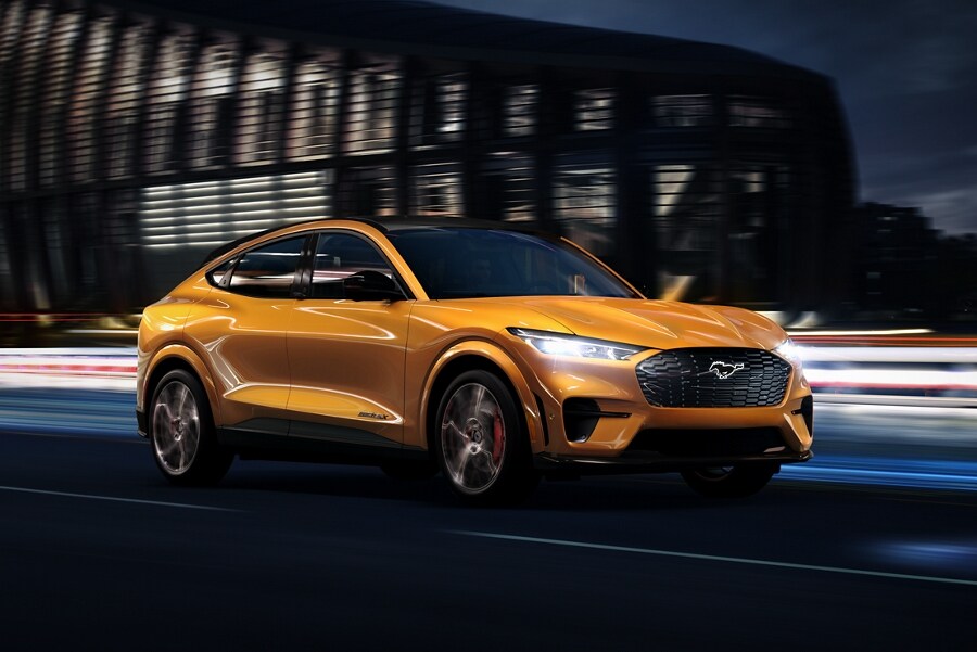 Cyber Orange 2023 Ford Mustang Mach-E® being driven on a highway past a stadium at night