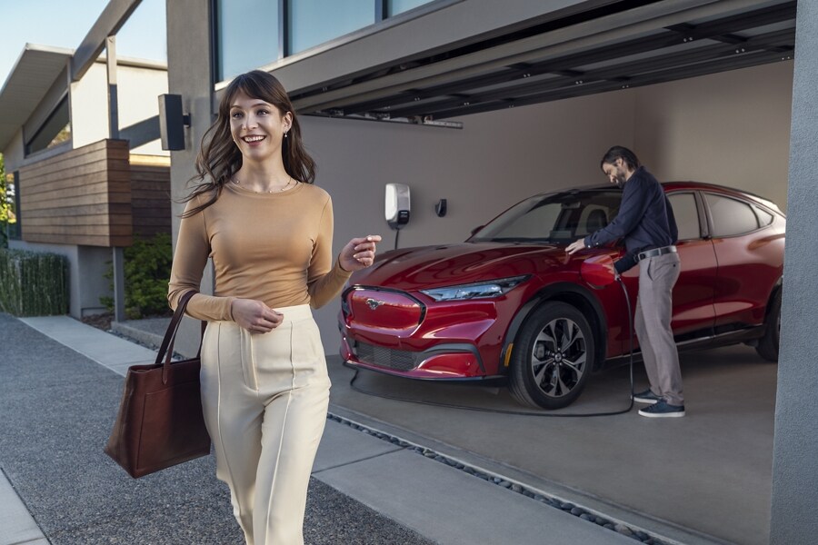 Mujer con un atuendo corporativo saliendo de un garaje con un hombre que está desenchufando un cargador de una Ford Mustang Mach-E® 2023