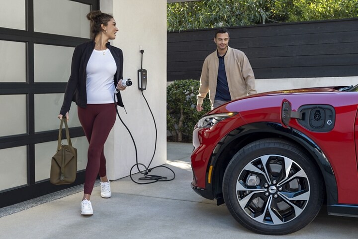 Mujer sosteniendo un cargador y mirando hacia atrás a un hombre que mira con pasión la parte delantera de una Ford Mustang Mach-E® 2023