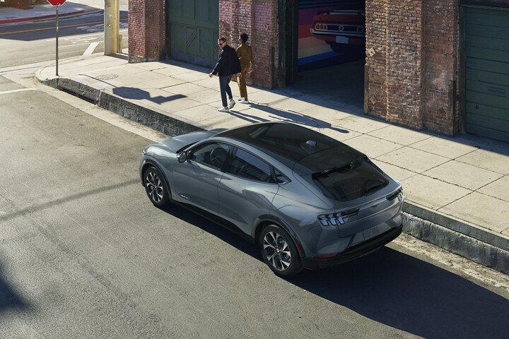 Una Ford Mustang Mach-E® 2023 estacionado en la calle con una pareja caminando y girando la cabeza para mirarla