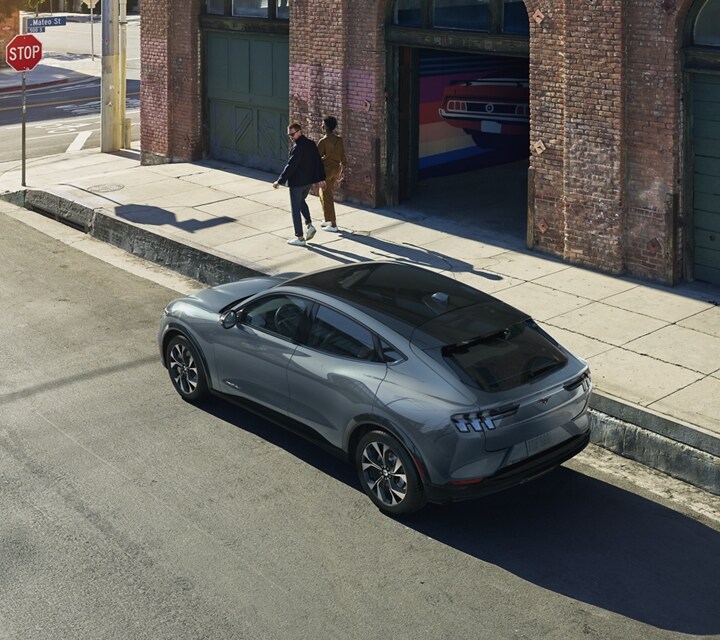 Woman walking with man who looks back at a 2023 Ford Mustang Mach-E SUV parked on a city street