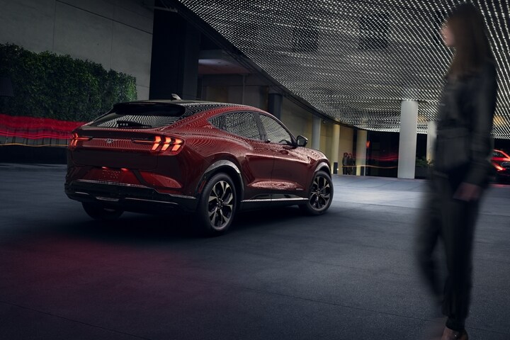 Mujer desenfocada mirando la parte trasera de la SUV Ford Mustang Mach-E® 2023 de noche con iluminación tenue de calle