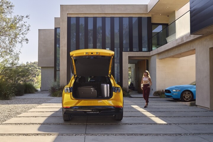 Rear end of the 2023 Ford Mustang Mach-E® parked in a driveway with a legacy Ford Mustang parked to the right
