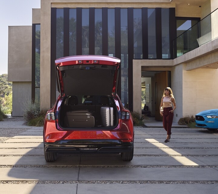 Rear end of the 2023 Ford Mustang Mach-E SUV parked in a driveway with a legacy Ford Mustang parked to the right