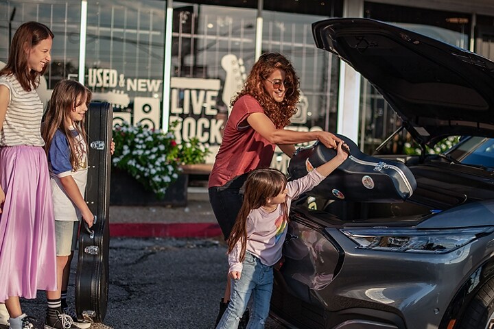 Una mujer ayuda a un niño a meter un instrumento musical en la cajuela delantera de una SUV Ford Mustang Mach-E® 2023