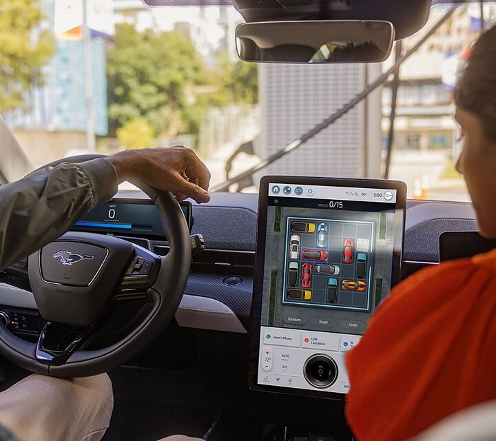 Two people inside a parked 2023 Ford Mustang Mach-E SUV with a game on the portrait touchscreen right