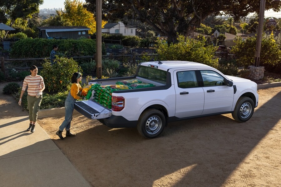 Two women unload supplies from the bed of a 2023 Ford Maverick® XL truck in Oxford White