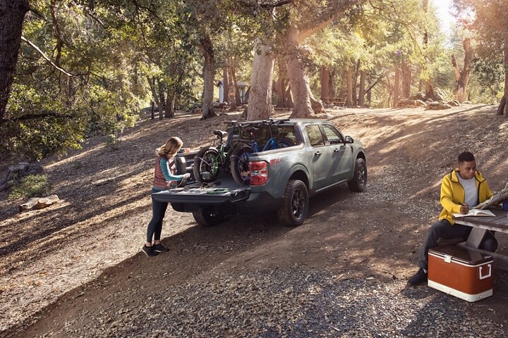 Woman at a campsite plugs an electric bike into the bed of a 2023 Ford Maverick® XLT model