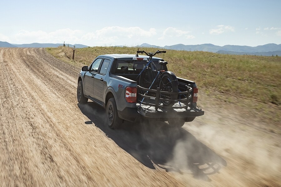 2023 Ford Maverick® truck with bed extender being driven on a dusty gravel road