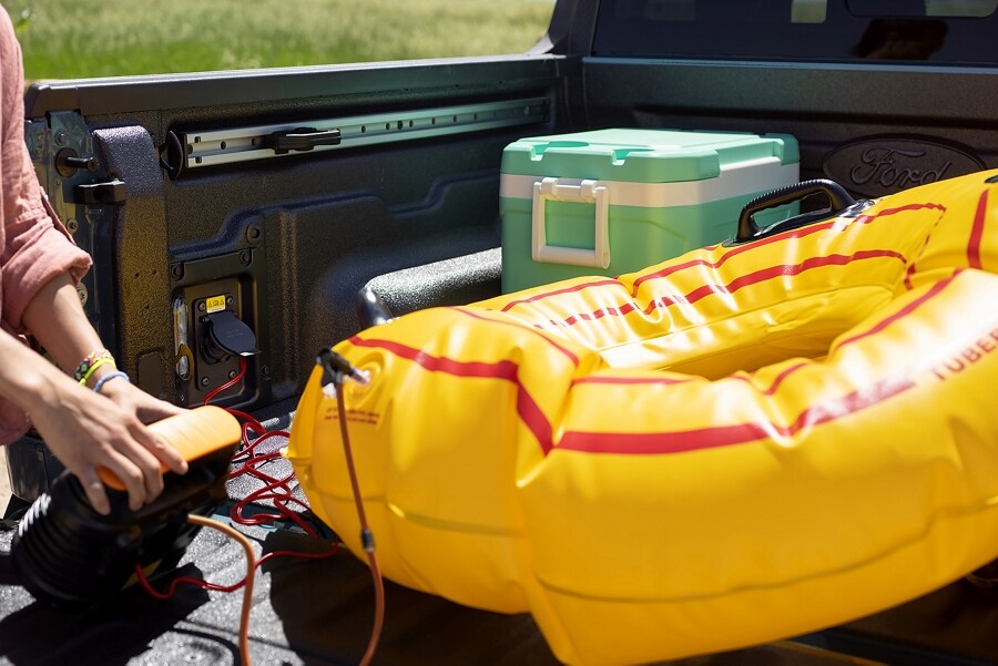 Una persona inflando un gomón para playa con un compresor de aire eléctrico enchufado en la plataforma de una camioneta Ford Maverick® 2023