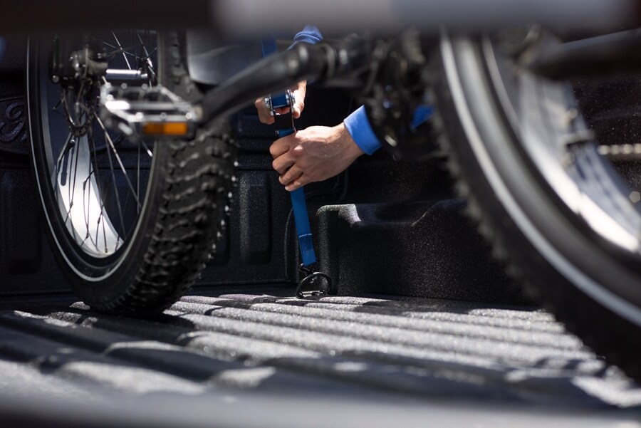 Un hombre sujeta la bicicleta con una correa de amarre en la plataforma de una camioneta Ford Maverick® 2023