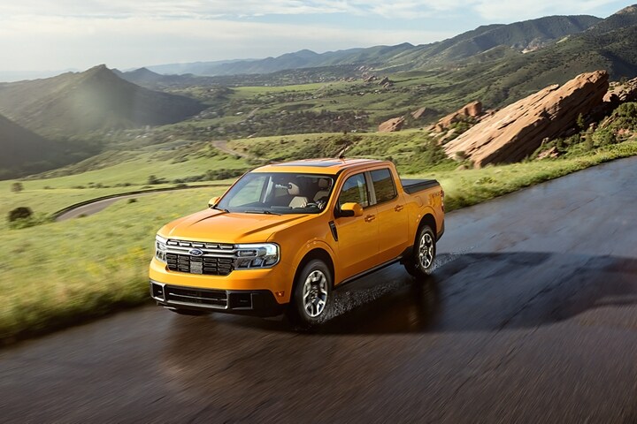 A 2023 Ford Maverick® in Cyber Orange driven on a road lined with grass and boulders