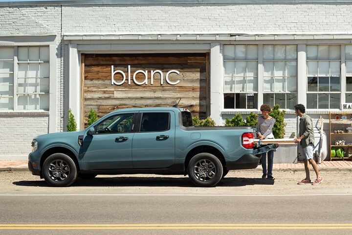 Dos personas cargan madera en la plataforma de una camioneta Ford Maverick® 2023 fuera de una moderna tienda para el hogar llamada Blanc