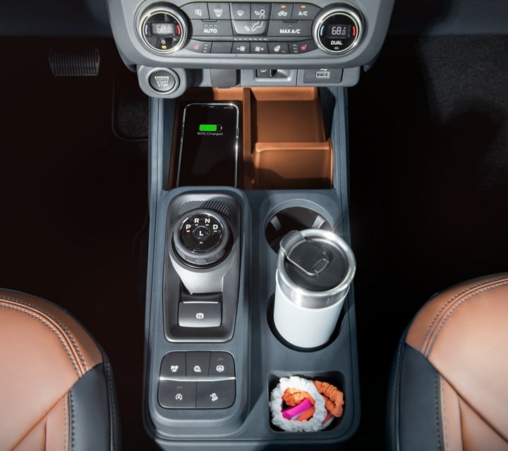 Vista superior del dial giratorio en palanca de cambios, el portavasos y un teléfono cargándose de manera inalámbrica en la Ford Maverick® 2023