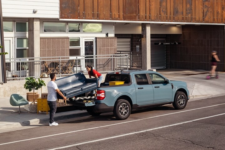 Two people unload a couch from the back of their 2023 Ford Maverick® truck in the color Area 51
