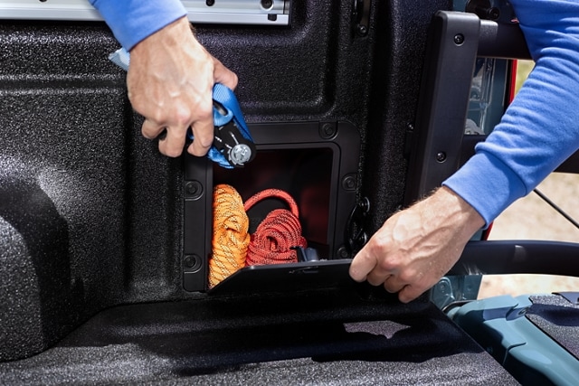 Un hombre coloca una correa de amarre dentro del almacenamiento de la plataforma de una camioneta Ford Maverick® 2023