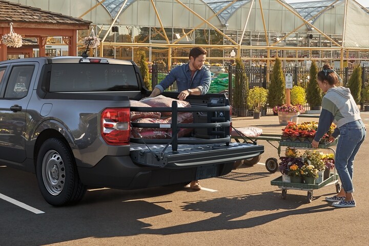 Two people putting flowers and bags of soil into the bed of a 2023 Ford Maverick® truck with available bed extender