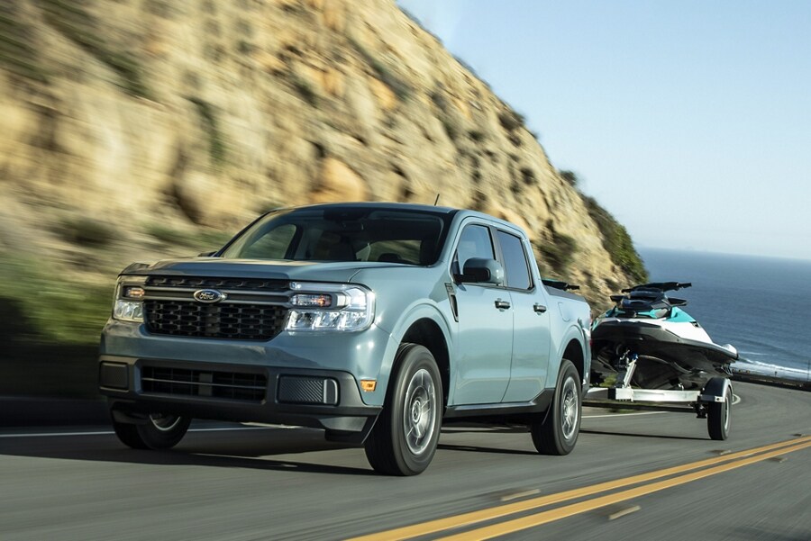 2023 Ford Maverick® truck pulling a personal watercraft on an inclined highway above a lake
