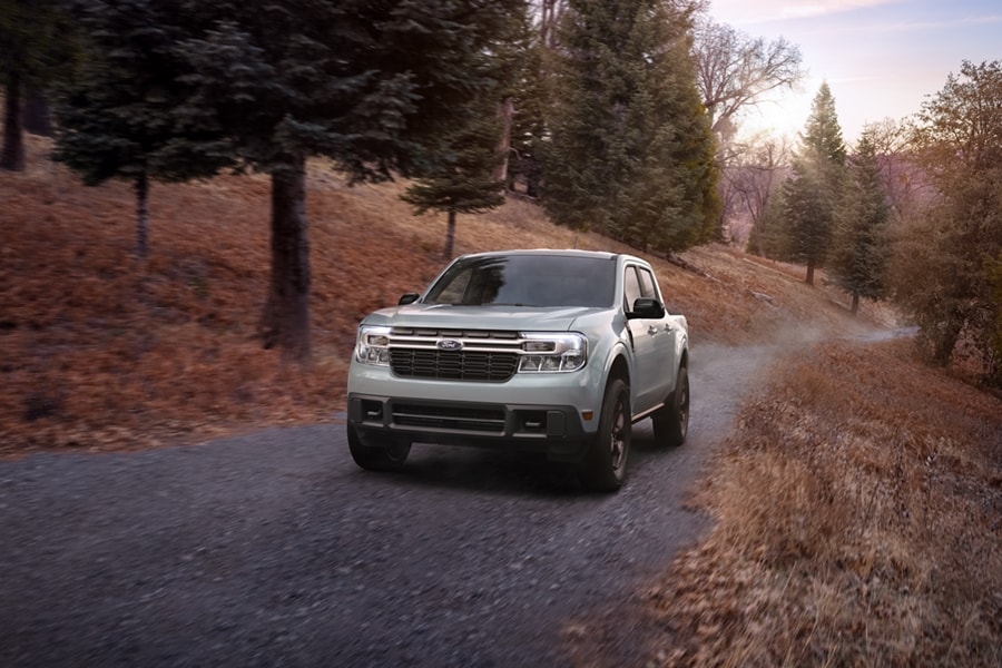 A 2024 Ford Maverick® truck with the FX4® Off-Road Package is being driven on a paved road in a scenic location