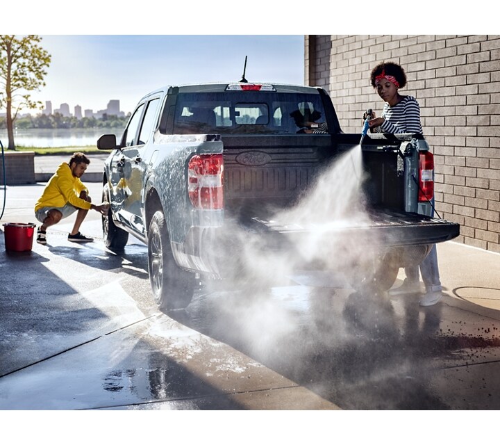 A 2024 Ford Maverick® truck in Azure Gray Metallic is being sprayed with water by two people at an outdoor carwash