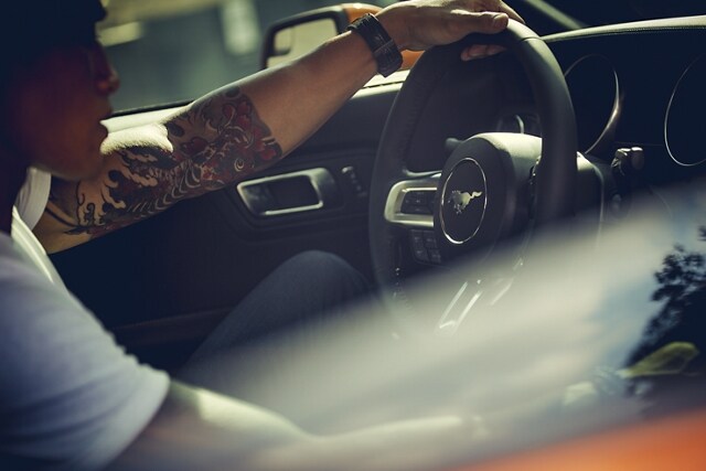 A man with tattoos behind the wheel of a 2021 Ford Mustang