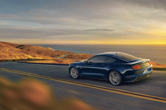 A 2021 Ford Mustang being driven on the open road with an ocean in the background