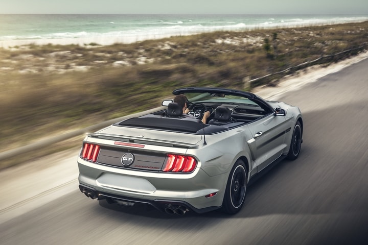 A 2021 Ford Mustang convertible traveling down a highway near a beach