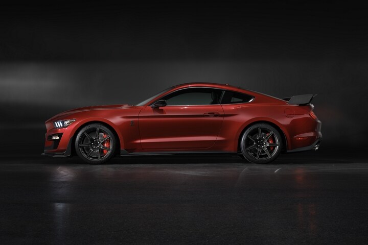 Side view of a 2021 Ford Mustang G T 500 in rapid red in a dark room