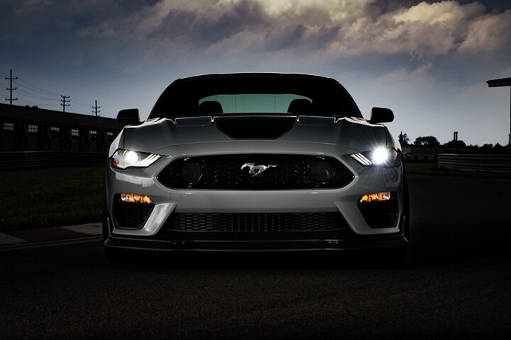 Un Ford Mustang® Mach 1® Coupe 2023 al atardecer con los faros delanteros encendidos