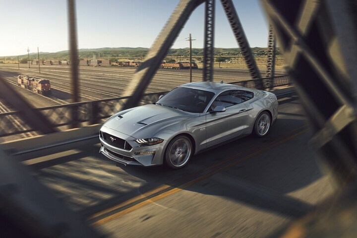 Un modelo Ford Mustang® GT 2023 en Iconic Silver Metallic conduciendo por un puente de metal sobre las vías del tren