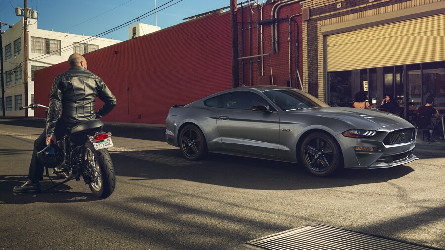 Una persona en una motocicleta admirando una Ford Mustang® Coupe 2023 estacionada