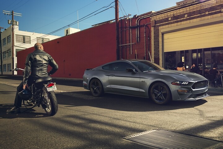 Una persona en una motocicleta admirando una Ford Mustang® Coupe 2023 estacionada en una calle urbana