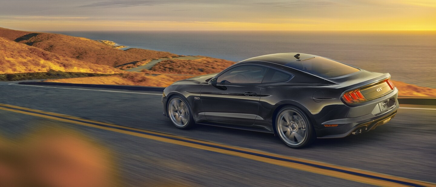 Un Ford Mustang® 2023 cupé en Shadow Black circulando por una carretera junto al mar