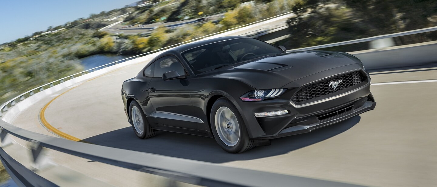 Una Ford Mustang® Coupe 2023 en Shadow Black circulando por una curva en un camino de montaña