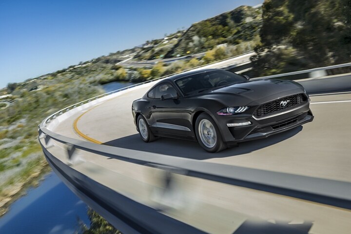 A 2023 Ford Mustang® coupe being driven around a curve over a valley