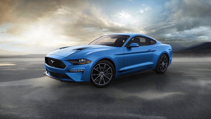 Una Ford Mustang® Coupe 2023 en Grabber Blue Metallic en la costa del mar con montañas de fondo