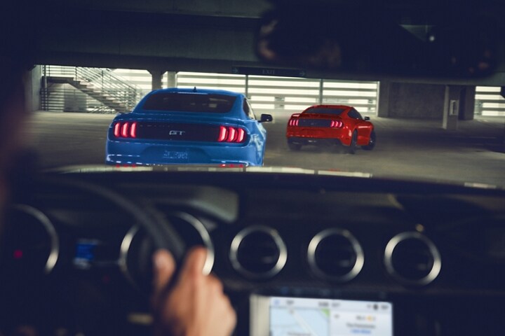 View through a 2023 Ford Mustang® coupe windshield being driven through a parking garage following two other Mustang models