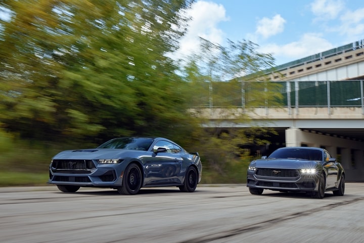2024 Mustang® GT coupe in Vapor Blue Metallic and an EcoBoost® coupe in Carbonized Gray Metallic being driven on a road