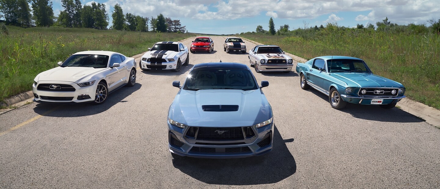 2024 Ford Mustang® coupe in the foreground with several older Mustang vehicles parked on a road behind it