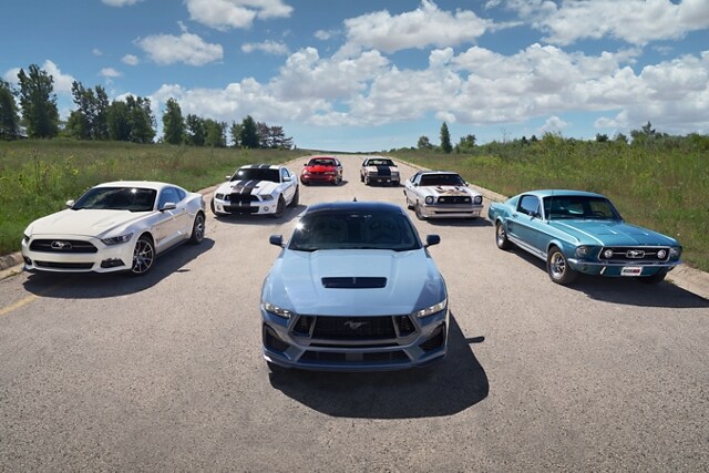 2024 Ford Mustang® coupe in the foreground with several older Mustang vehicles parked on a road behind it