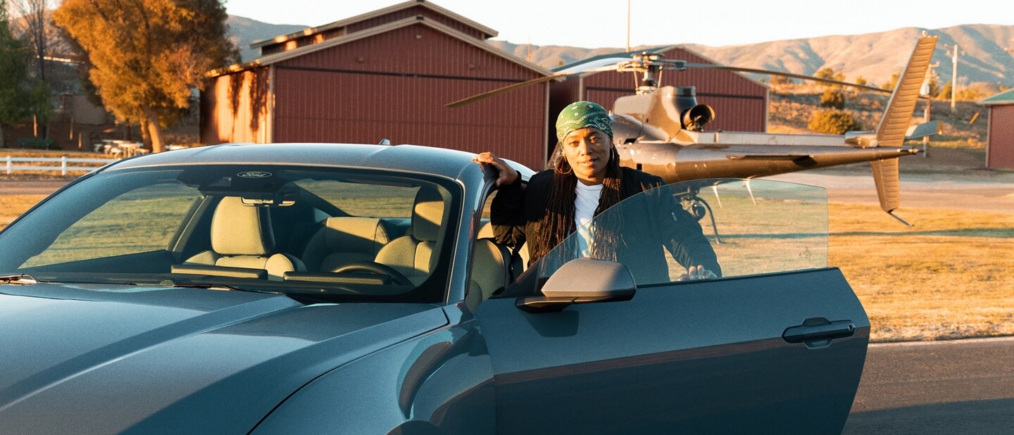 Dee Bryant standing near the open driver-side door of a parked 2024 Ford Mustang® coupe